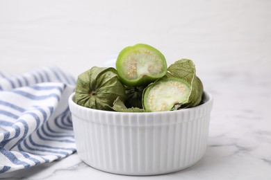 Fresh green tomatillos with husk in bowl on light marble table, closeup