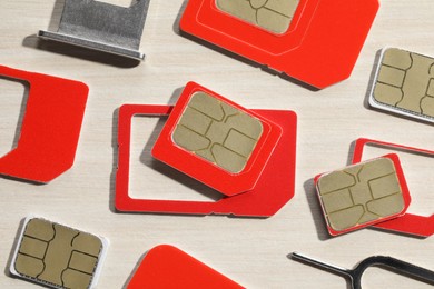 Different SIM cards, ejector and tray on wooden background, flat lay