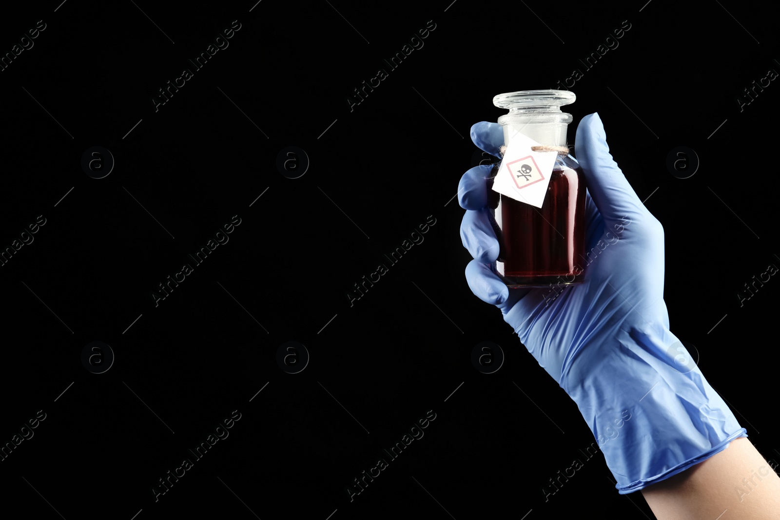 Photo of Woman in gloves holding glass bottle of poison with warning sign on black background, closeup. Space for text