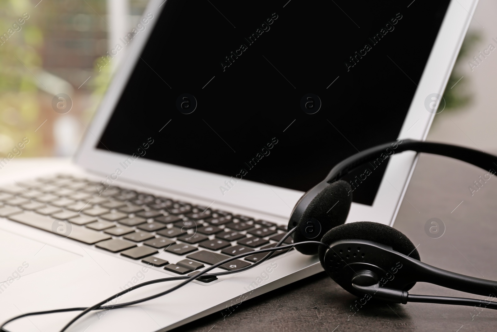 Photo of Modern laptop and headset on table. Technical support concept