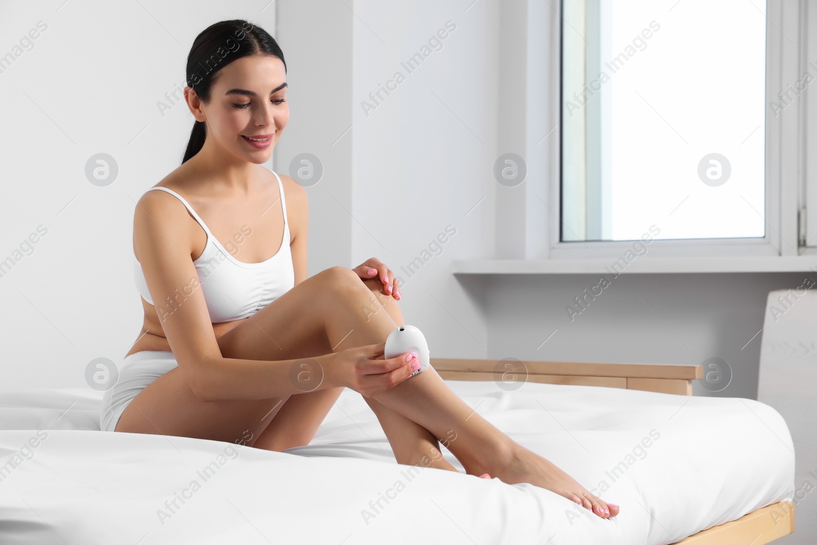 Photo of Young woman epilating her legs on bed