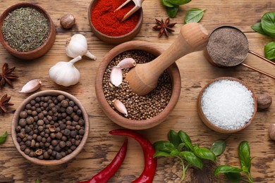 Mortar with pestle and different spices on wooden table, flat lay