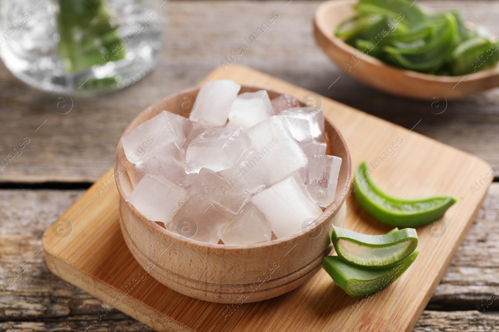 Photo of Aloe vera gel and slices of plant on wooden table, closeup