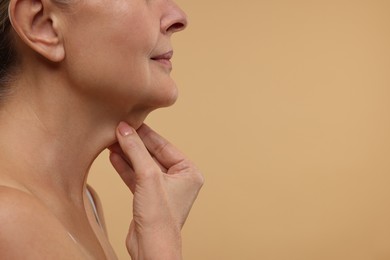 Mature woman touching her neck on beige background, closeup. Space for text