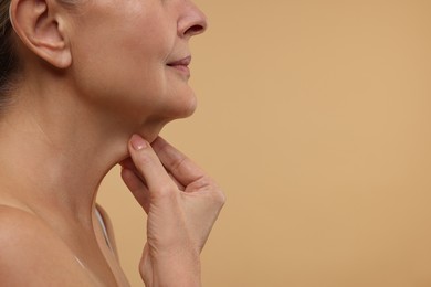 Photo of Mature woman touching her neck on beige background, closeup. Space for text