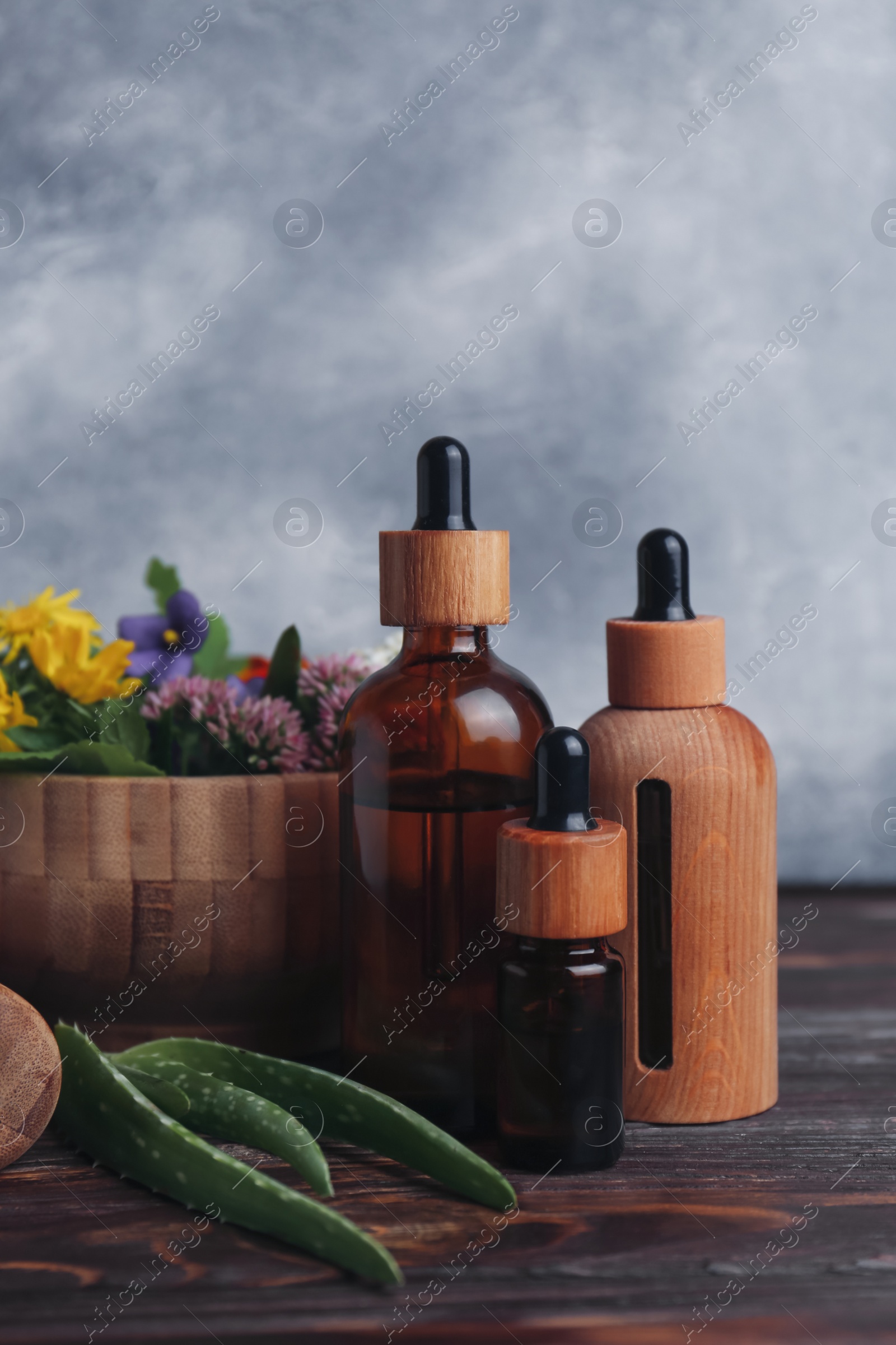 Photo of Glass bottles of aromatic essential oil and mortar with different herbs on wooden table