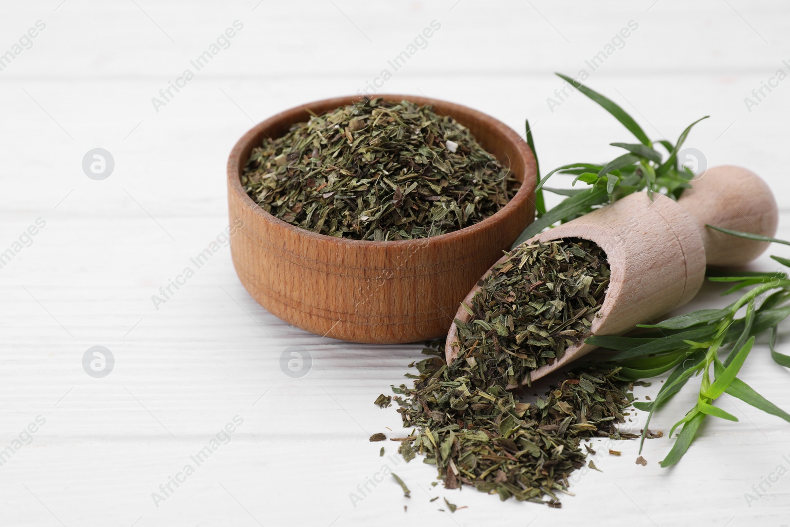 Photo of Bowl of dry tarragon, scoop and fresh leaves on white wooden table