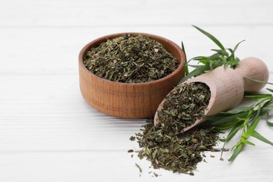 Bowl of dry tarragon, scoop and fresh leaves on white wooden table