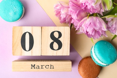 Photo of Wooden block calendar with date 8th of March, tulips and macarons on color background, flat lay. International Women's Day