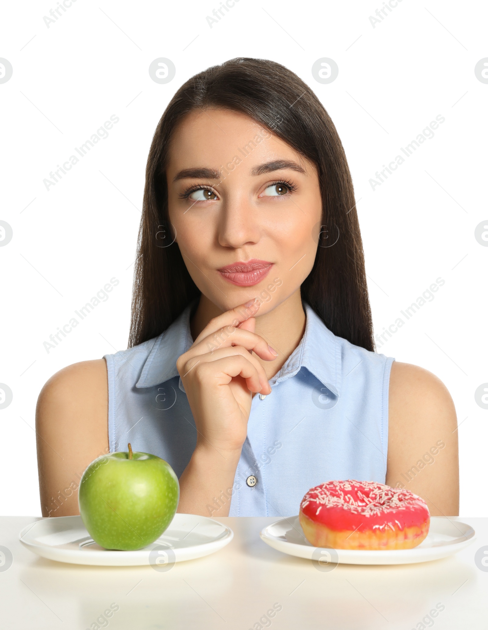 Photo of Doubtful woman choosing between apple and doughnut at table on white background