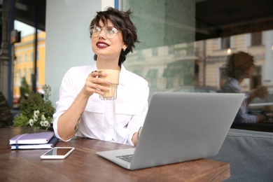 Photo of Young woman working with laptop at desk in cafe