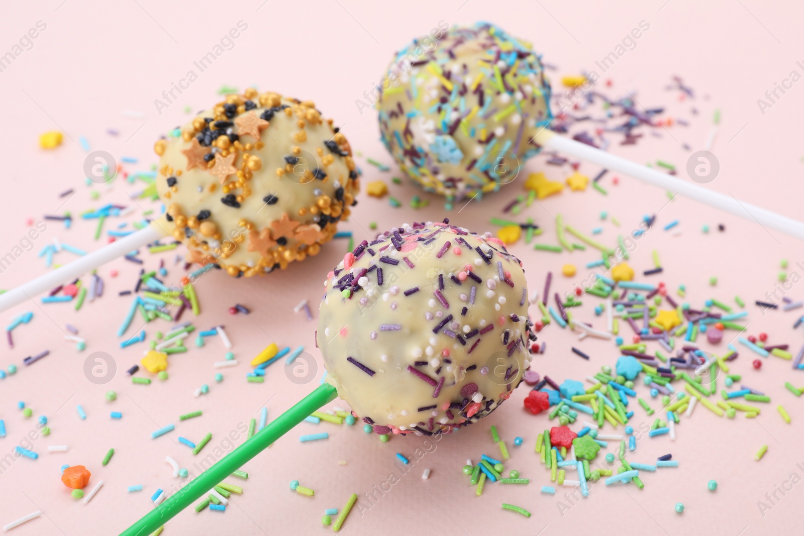 Photo of Delicious confectionery. Sweet cake pops decorated with sprinkles on pale pink background, closeup