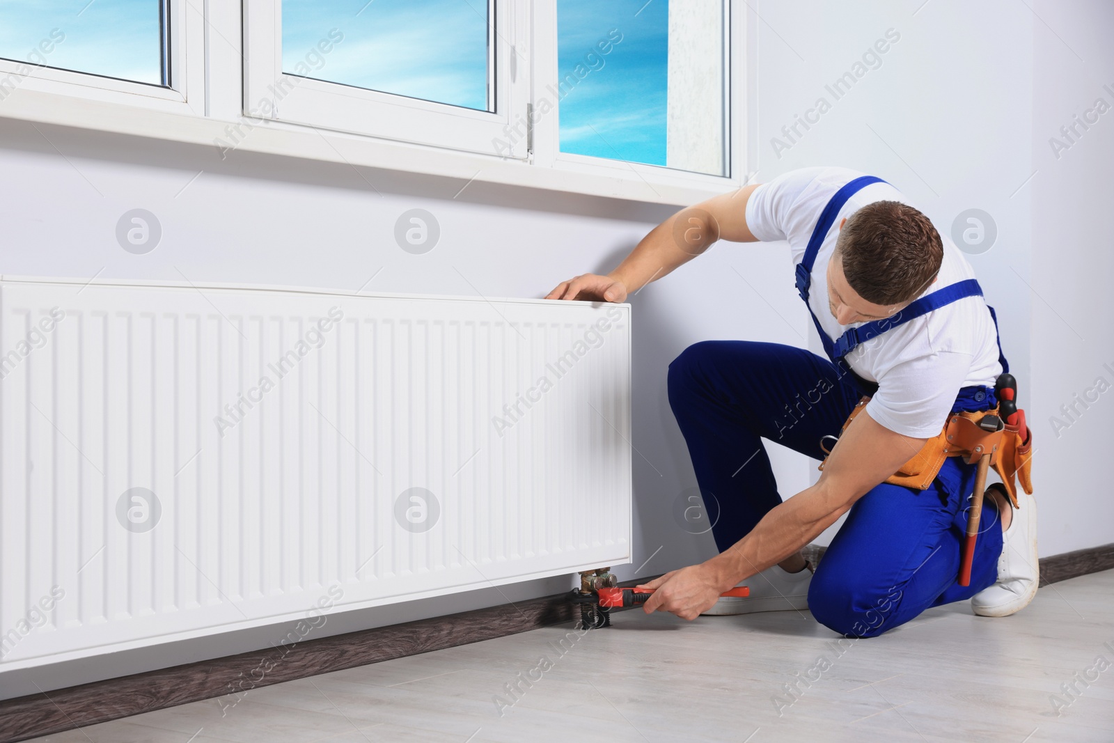 Photo of Professional plumber using adjustable wrench for installing new heating radiator in room