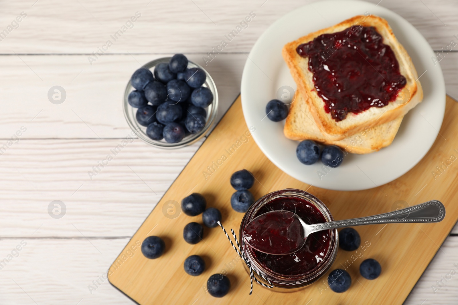 Photo of Delicious toast with blueberry jam and fresh berries on white wooden table, flat lay