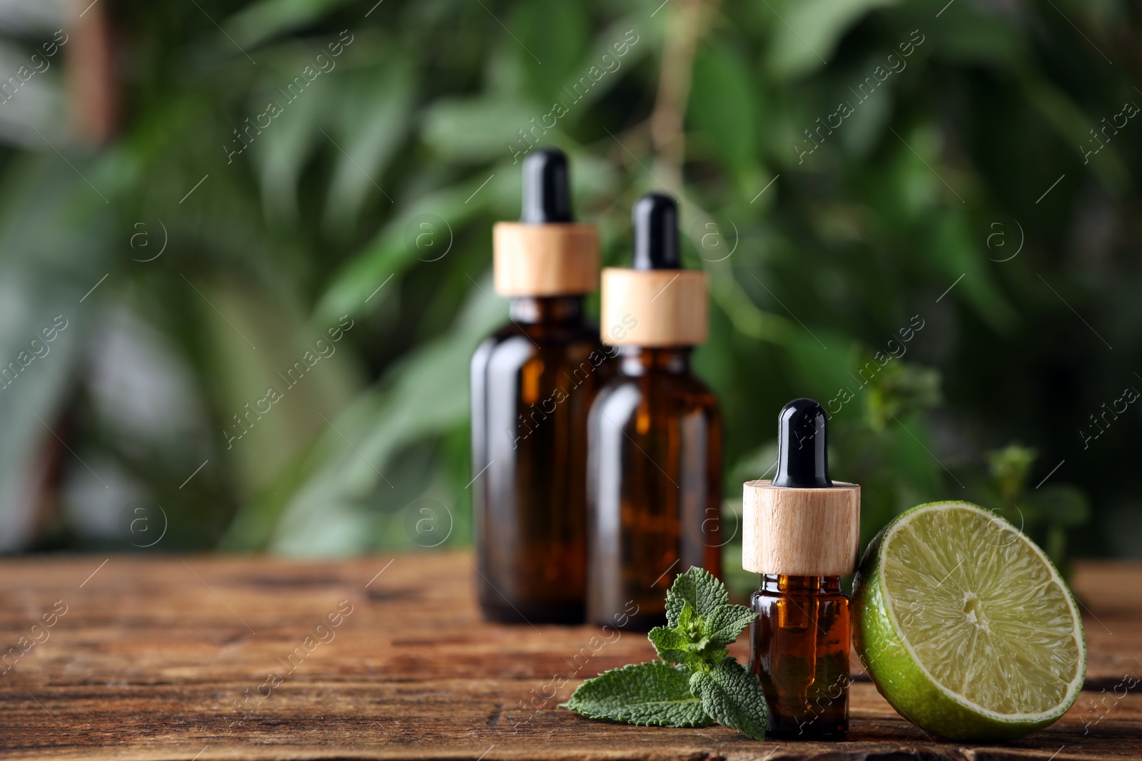 Photo of Bottles of essential oil, lime and fresh mint on wooden table against blurred background. Space for text