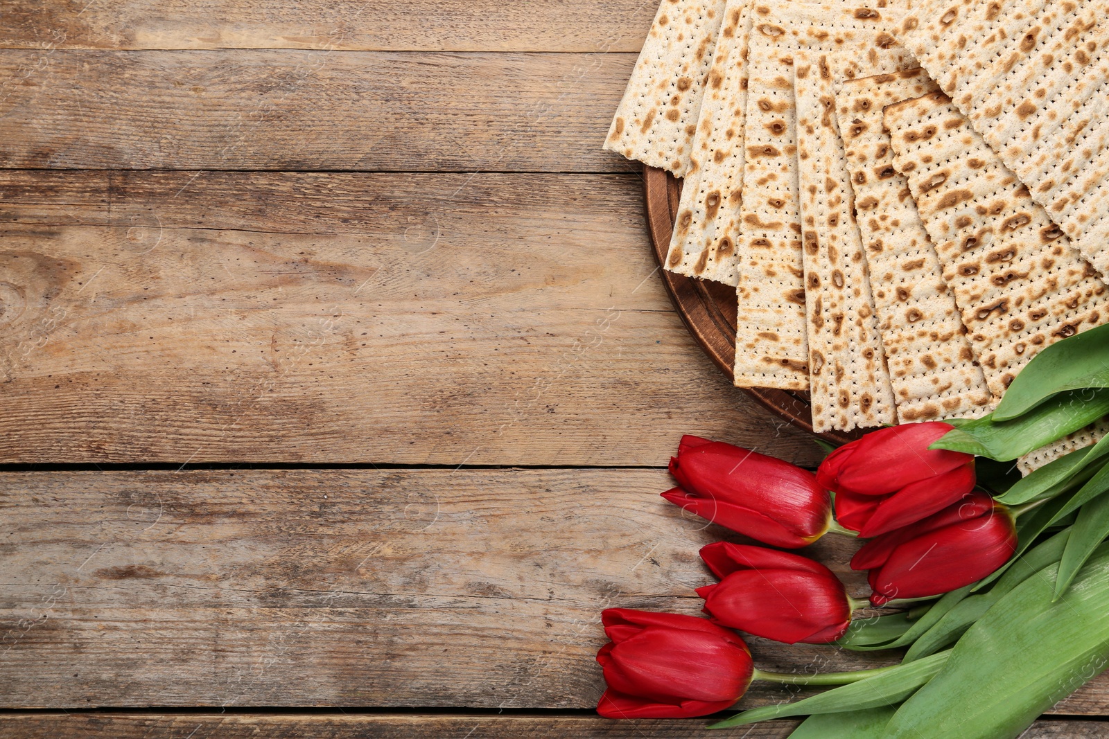 Photo of Tasty matzos and flowers on wooden table, flat lay with space for text. Passover (Pesach) Seder