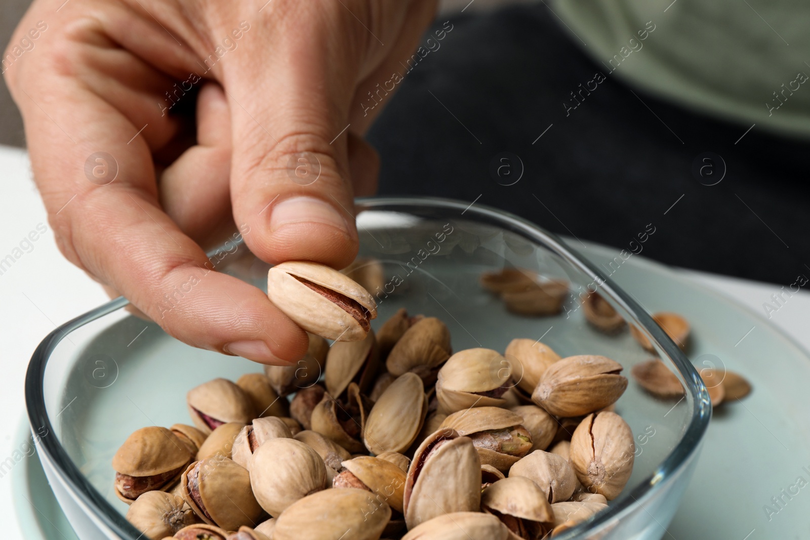 Photo of Woman taking tasty roasted pistachio nut from glass bowl at table, closeup