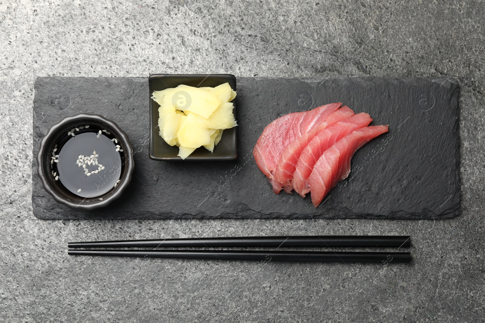 Photo of Tasty sashimi (pieces of fresh raw tuna) served with soy sauce and ginger slices on gray table, flat lay