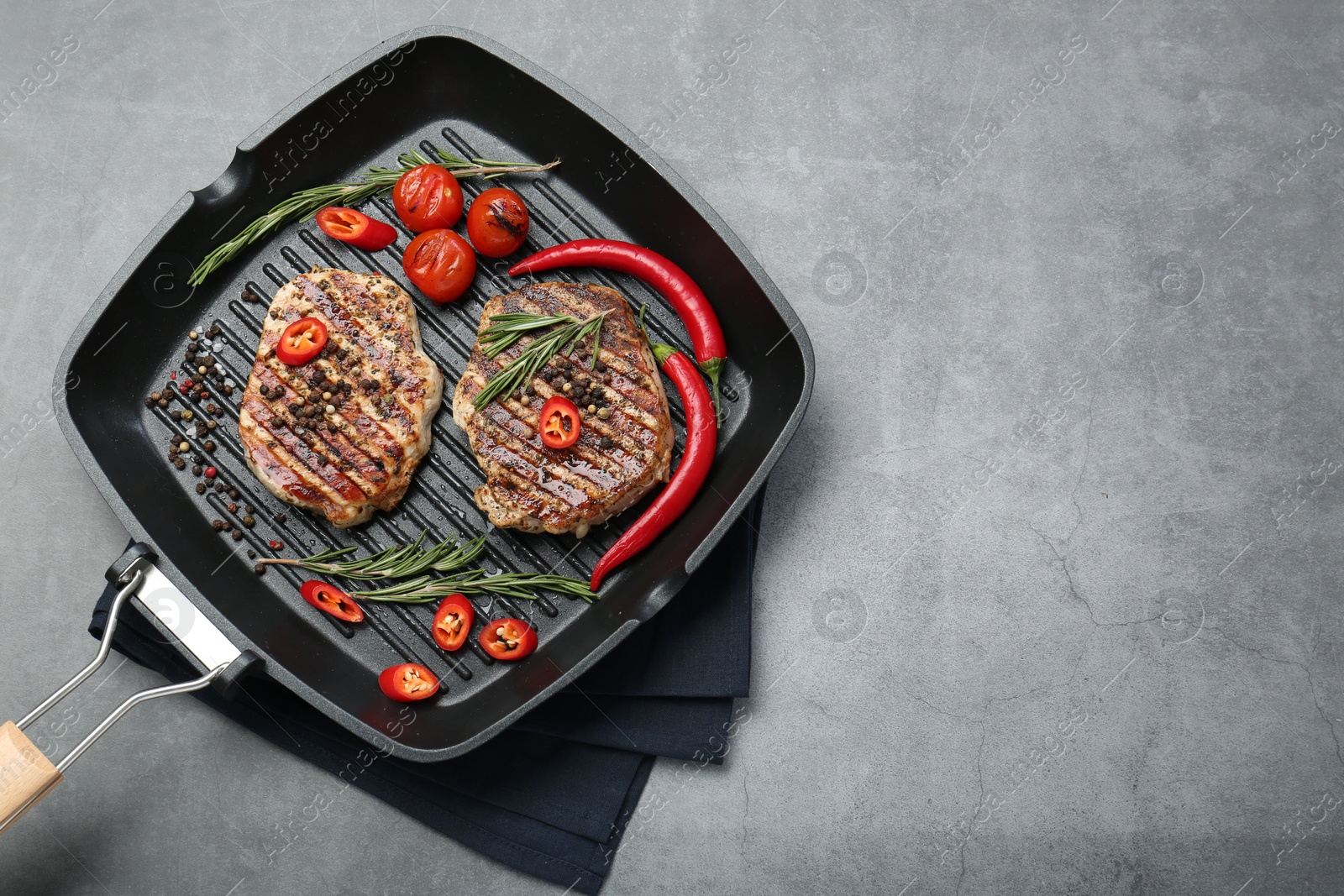 Photo of Grill pan with delicious pork steaks, spices and vegetables on grey table, top view. Space for text