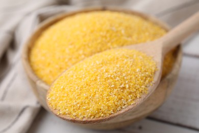 Raw cornmeal in bowl and spoon on light wooden table, selective focus