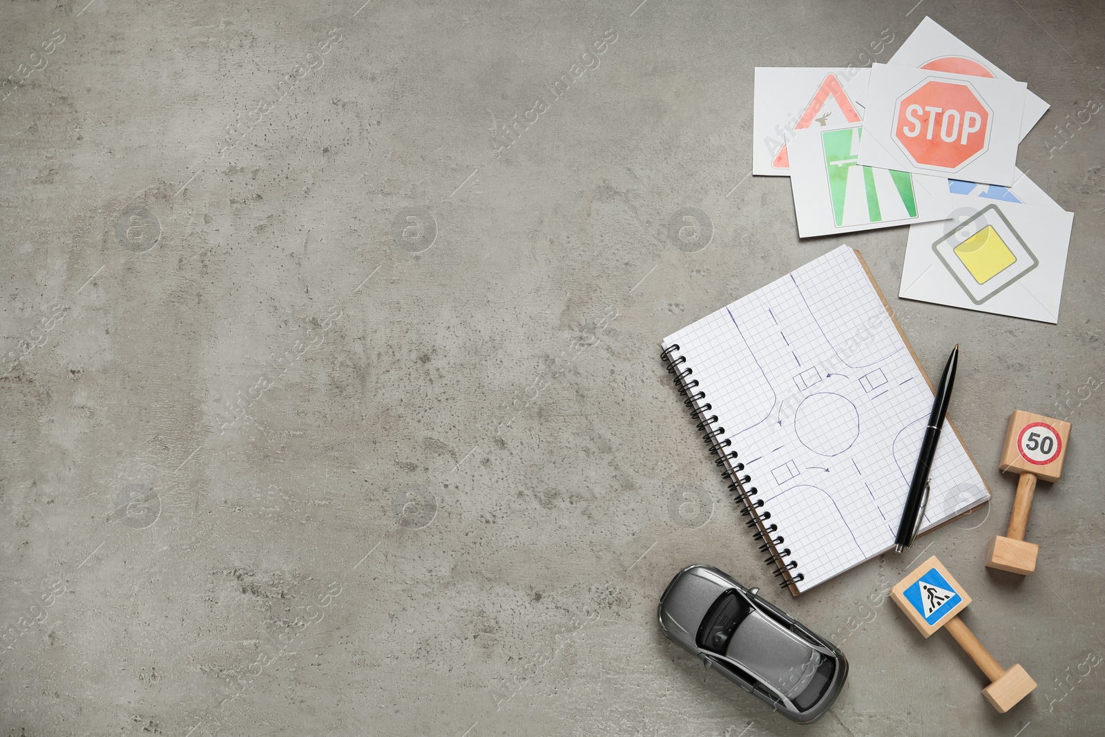 Photo of Many different road signs, notebook and toy car on grey background, flat lay with space for text. Driving school