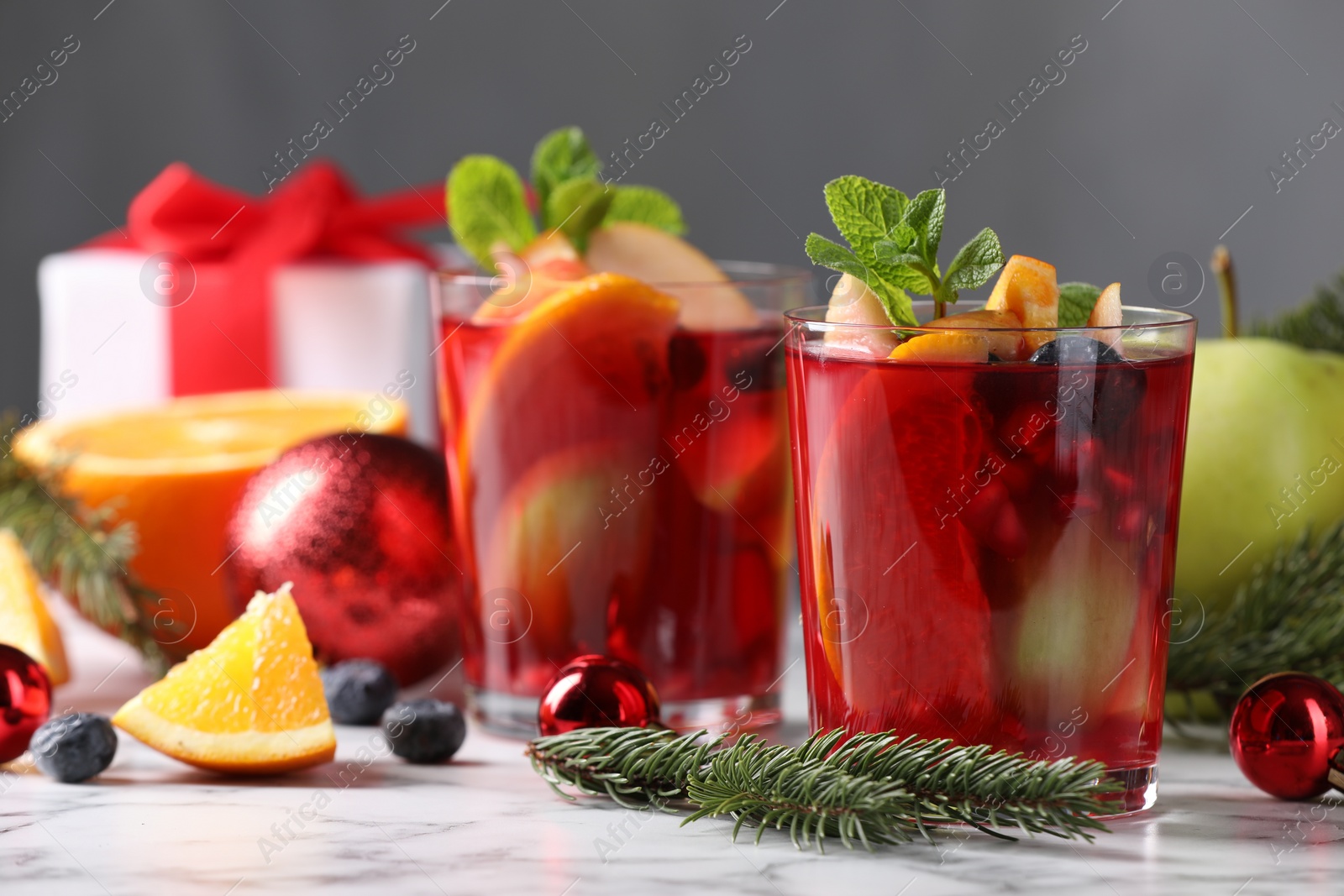 Photo of Aromatic Sangria drink in glasses, ingredients and Christmas decor on white marble table
