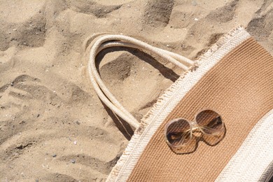 Photo of Sunglasses with straw bag on sand, top view. Beach accessories
