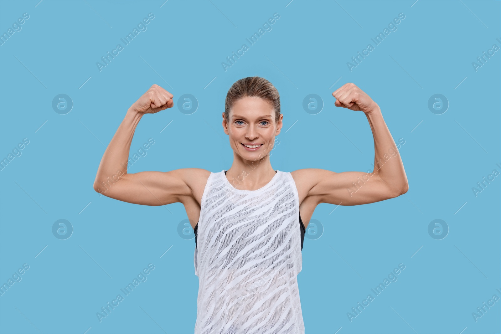 Photo of Portrait of sportswoman showing muscles on light blue background