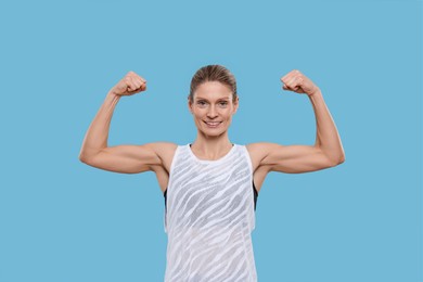 Photo of Portraitsportswoman showing muscles on light blue background