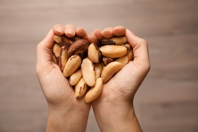 Photo of Woman holding Brazil nuts in hands on blurred background, top view
