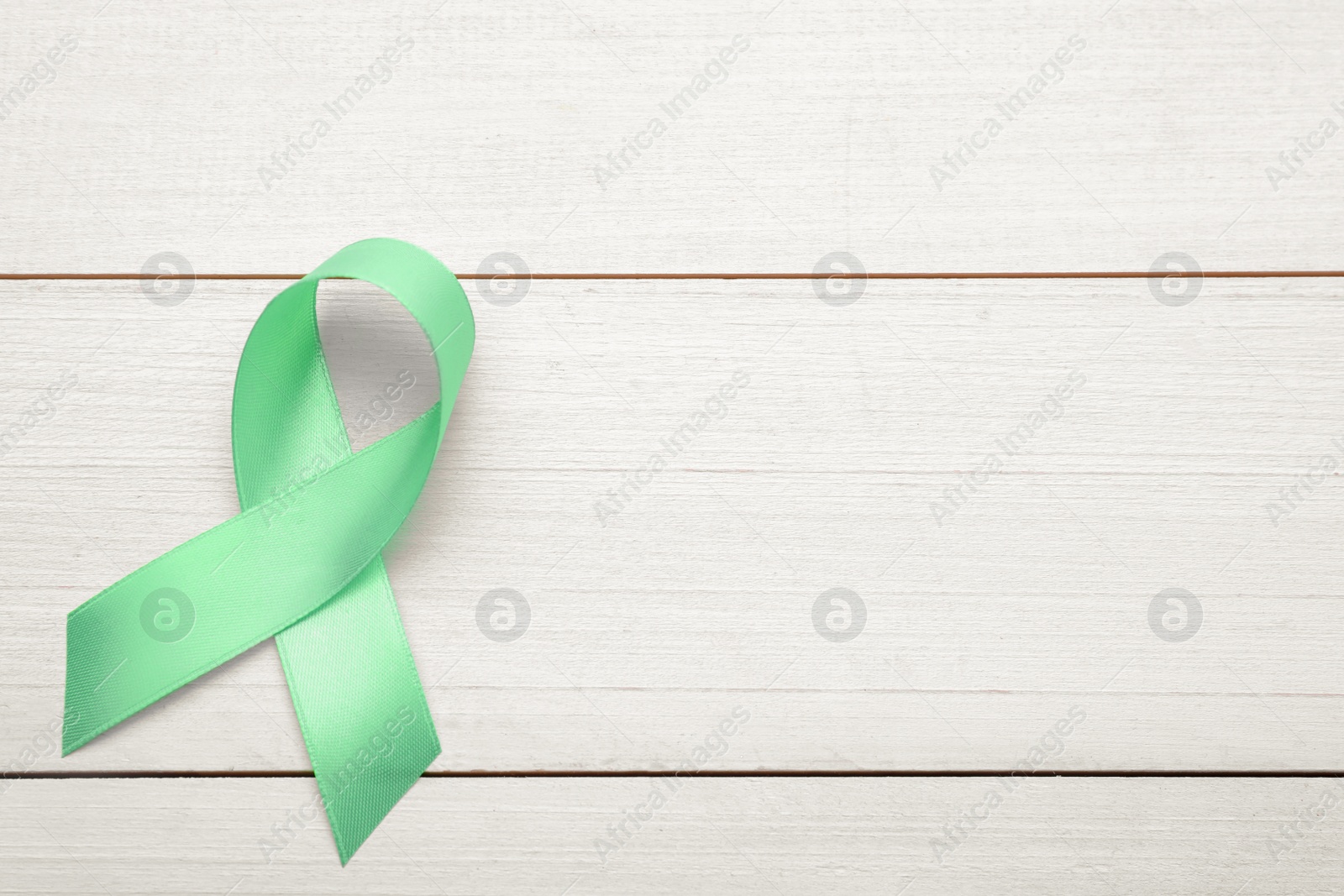 Photo of World Mental Health Day. Green ribbon on white wooden background, top view with space for text