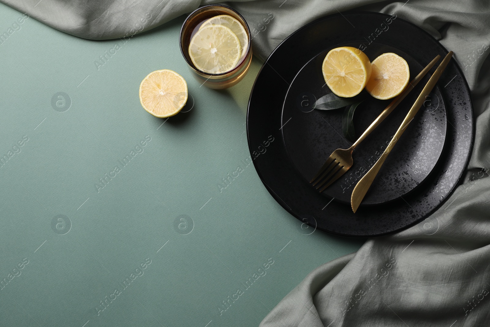 Photo of Stylish table setting. Plates, cutlery and tea with lemon on olive background, top view. Space for text