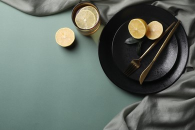 Stylish table setting. Plates, cutlery and tea with lemon on olive background, top view. Space for text