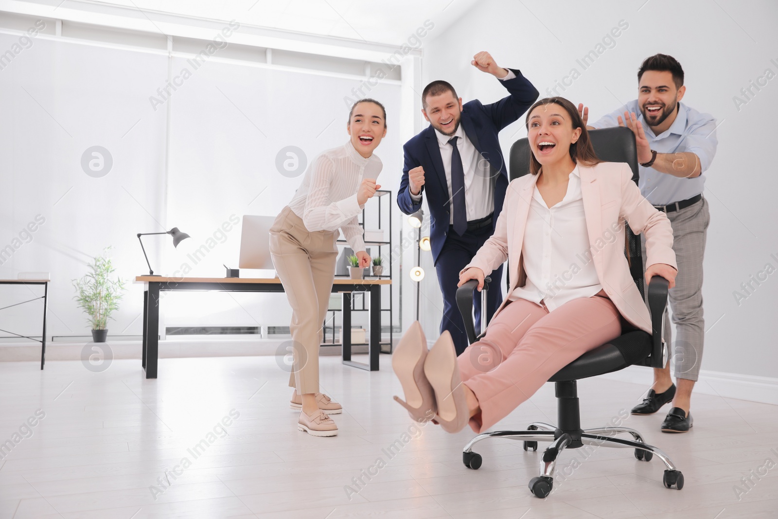 Photo of Office employee giving his colleague ride in chair at workplace. Space for text