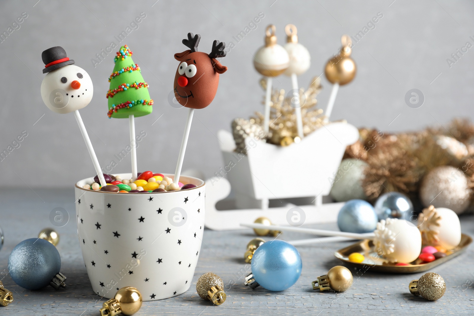 Photo of Delicious Christmas themed cake pops and festive decor on wooden table against grey background