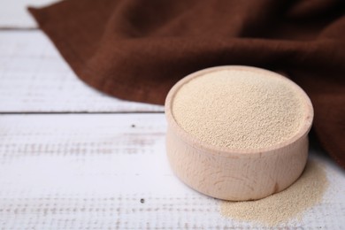 Photo of Granulated yeast in bowl on white wooden table, closeup. Space for text