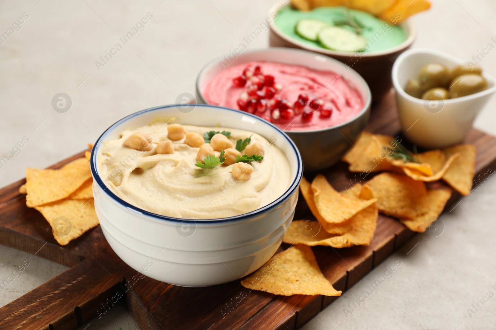 Photo of Different kinds of tasty hummus served with nachos on light table