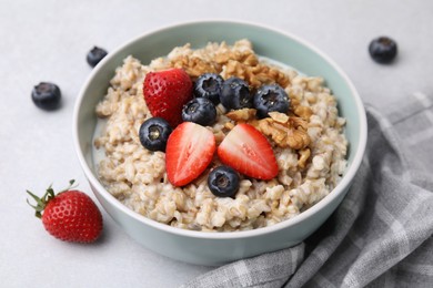 Photo of Tasty oatmeal with strawberries, blueberries and walnuts in bowl on grey table