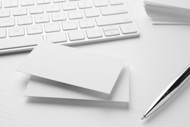 Blank business cards, keyboard and pen on white table. Mockup for design