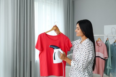 Woman steaming t-shirt on hanger at home. Space for text