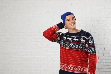 Photo of Portrait of young man in Christmas sweater and hat near white brick wall. Space for text