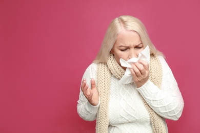 Mature woman sneezing on pink background, space for text. Cold symptoms