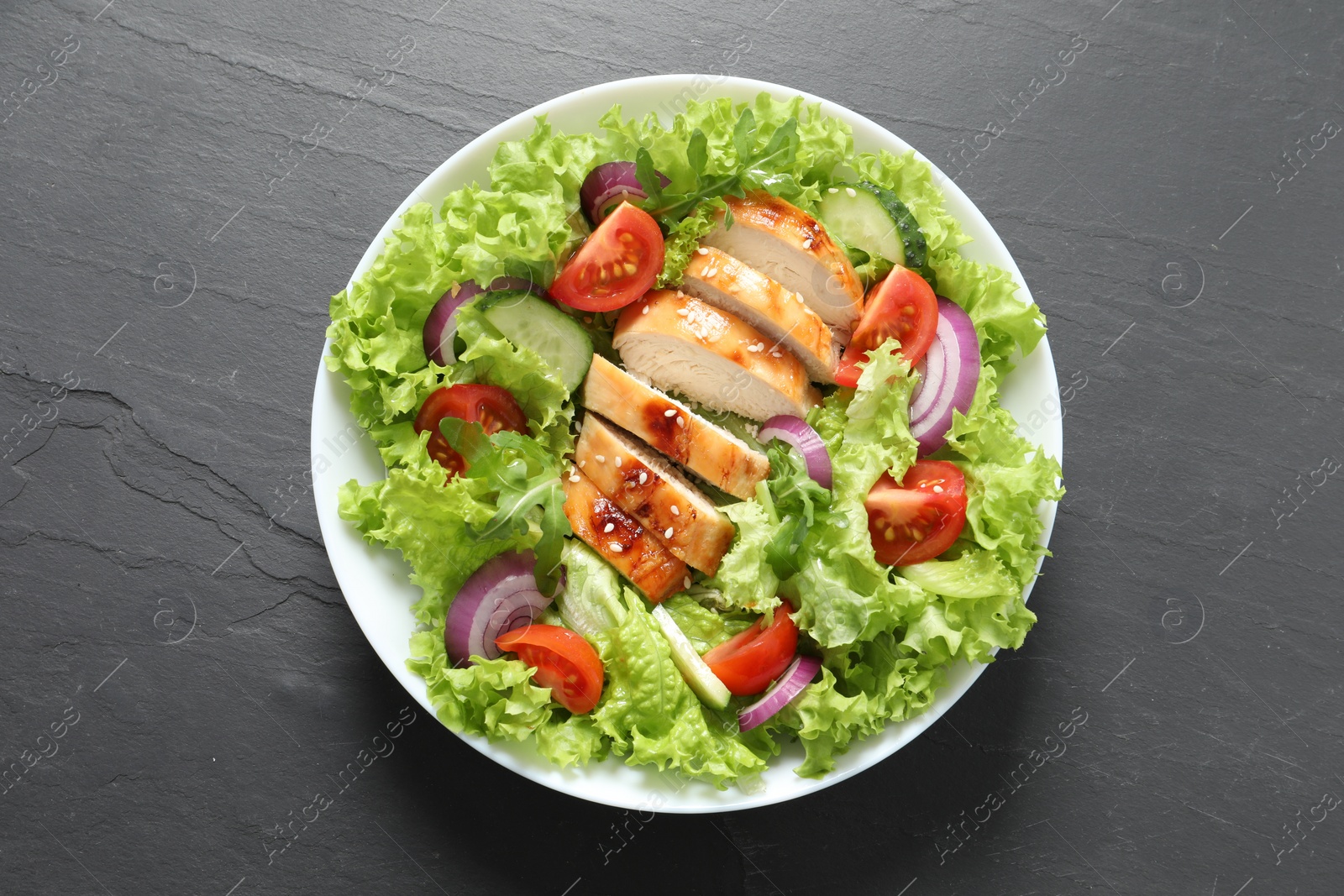 Photo of Delicious salad with chicken and vegetables on black table, top view