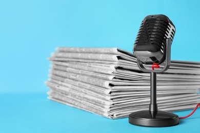 Photo of Newspapers and vintage microphone on light blue background. Journalist's work