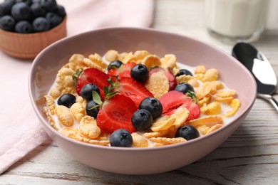 Photo of Bowl of tasty crispy corn flakes with milk and berries on white wooden table, closeup