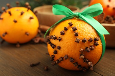 Photo of Pomander ball with green ribbon made of fresh tangerine and cloves on wooden table, closeup