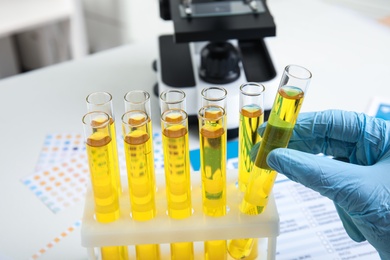 Doctor taking test tube with urine sample for analysis at white table, closeup