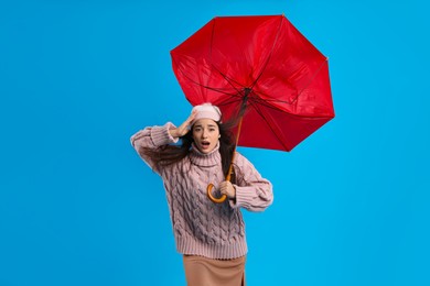Photo of Emotional woman with umbrella caught in gust of wind on light blue background
