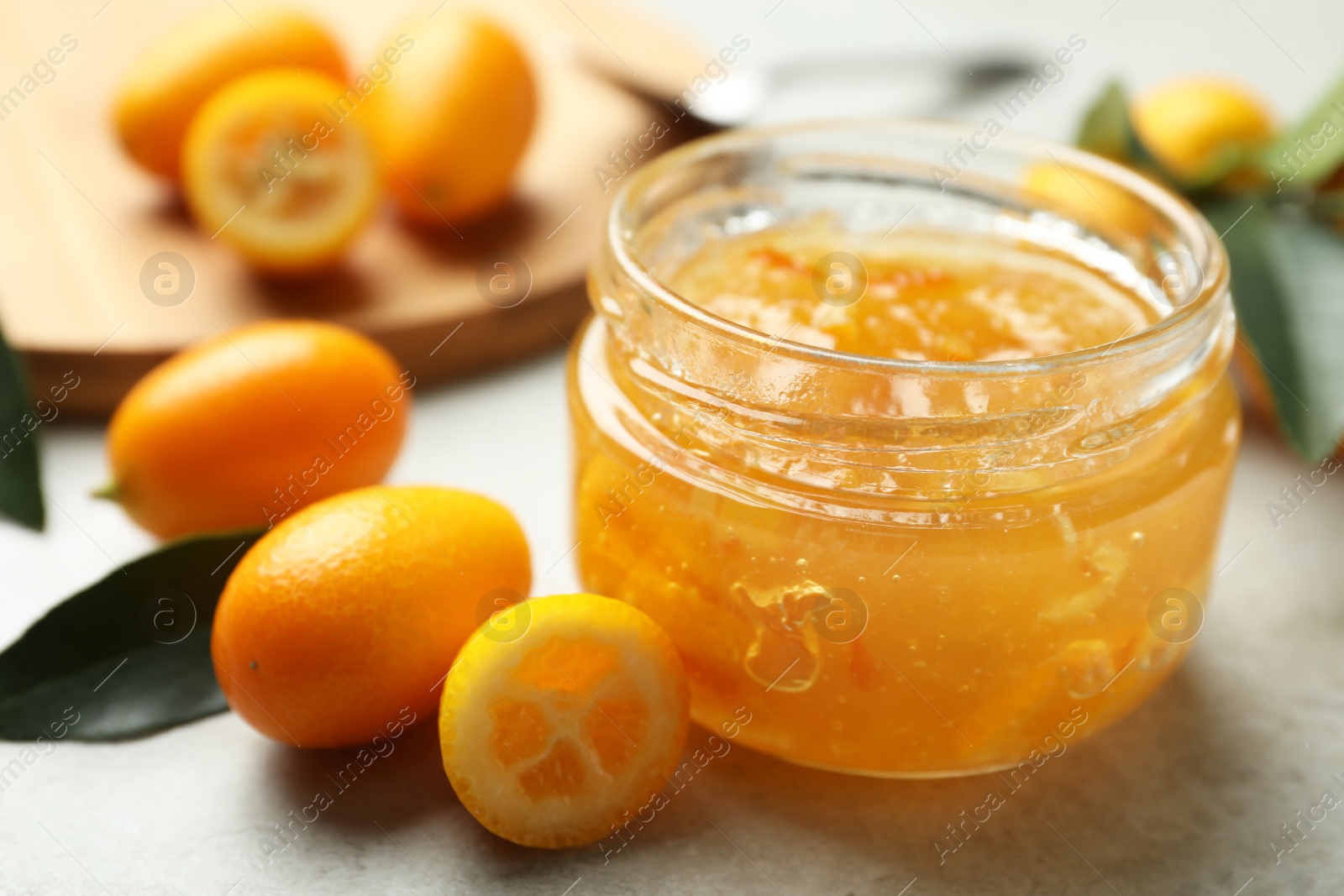 Photo of Delicious kumquat jam in jar and fresh fruits on light grey table, closeup. Space for text