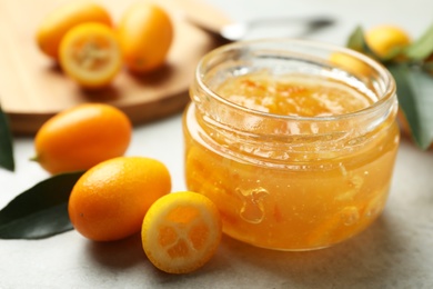 Delicious kumquat jam in jar and fresh fruits on light grey table, closeup. Space for text